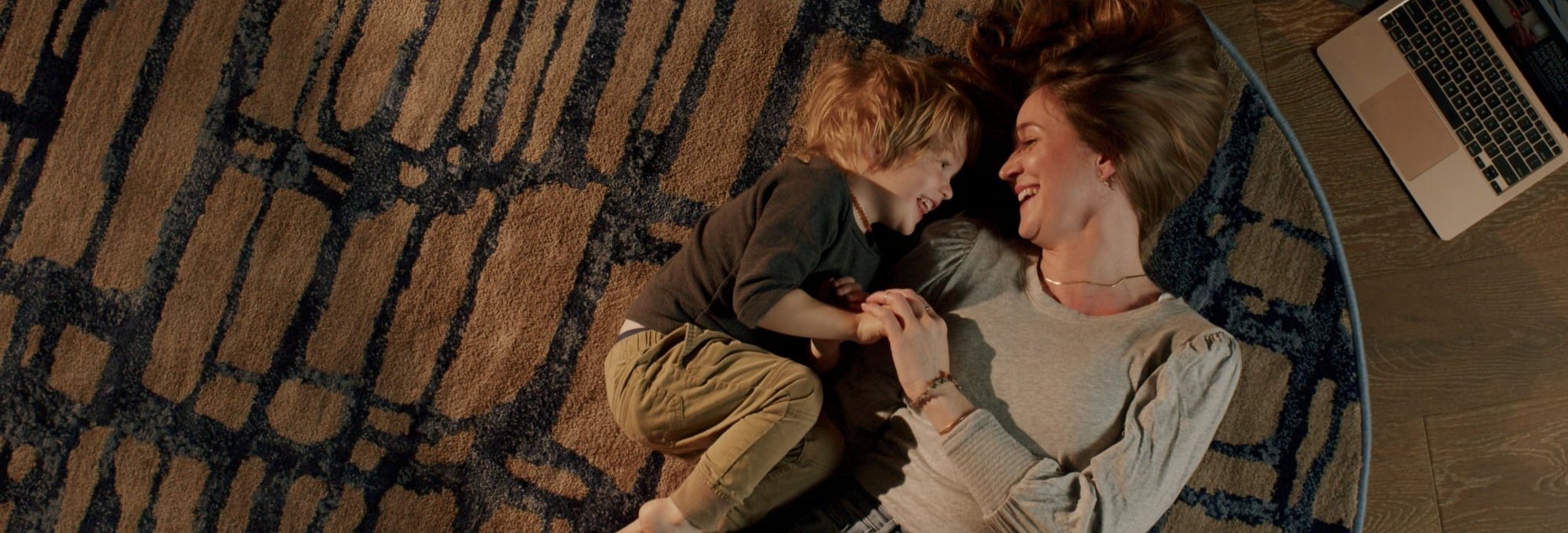 Happy Mother and child laying on a patterned black and brown area rug