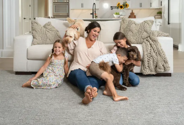 Mother and children playing with a family dog in a living room with cozy carpet